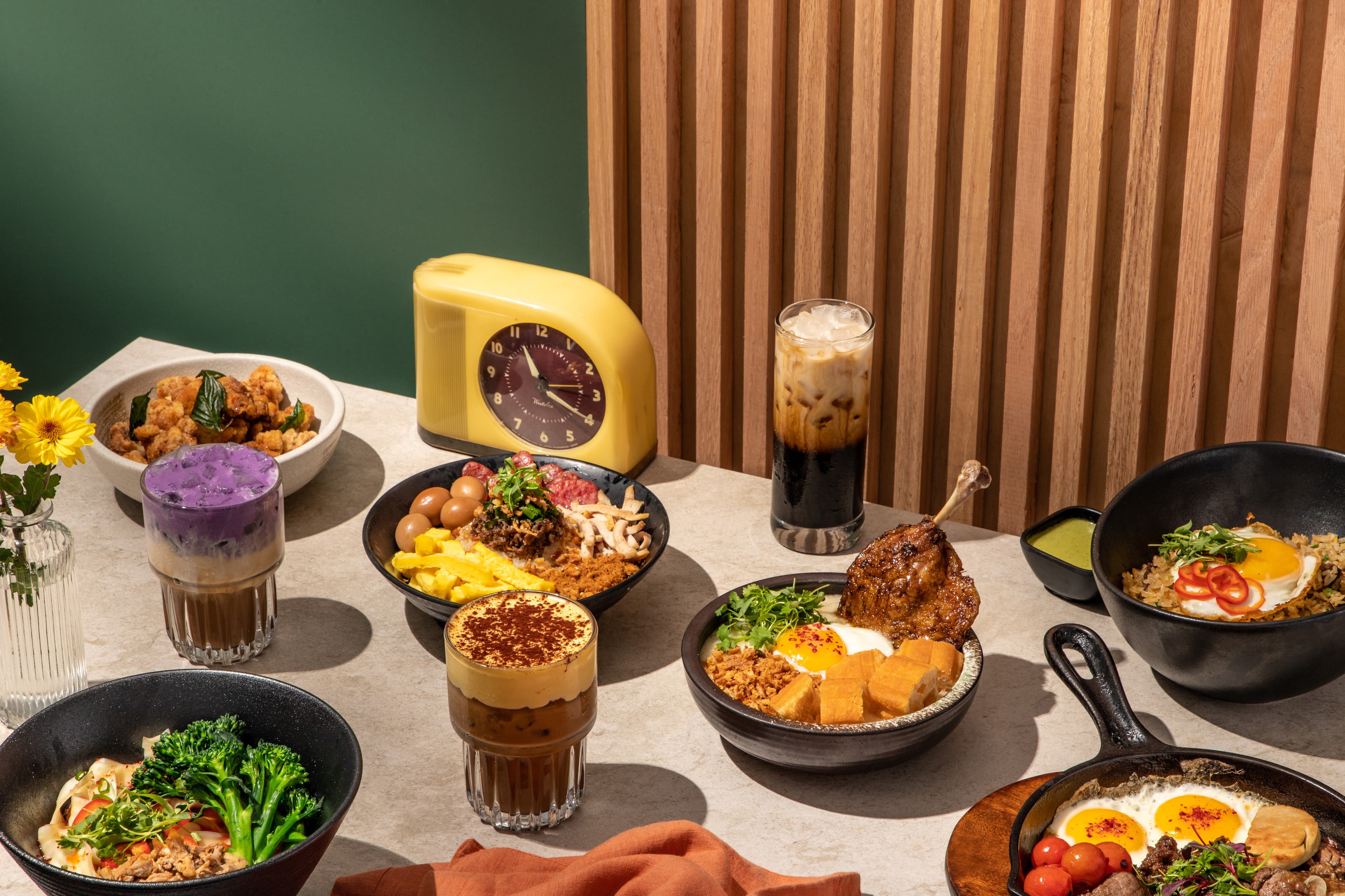 An overhead spread of Vietnamese-inspired dishes and drinks featuring banh mi chao with a sunny-side egg, beef tongue fried rice, egg coffee, ube coffee, and other signature plates arranged on a modern table setting.