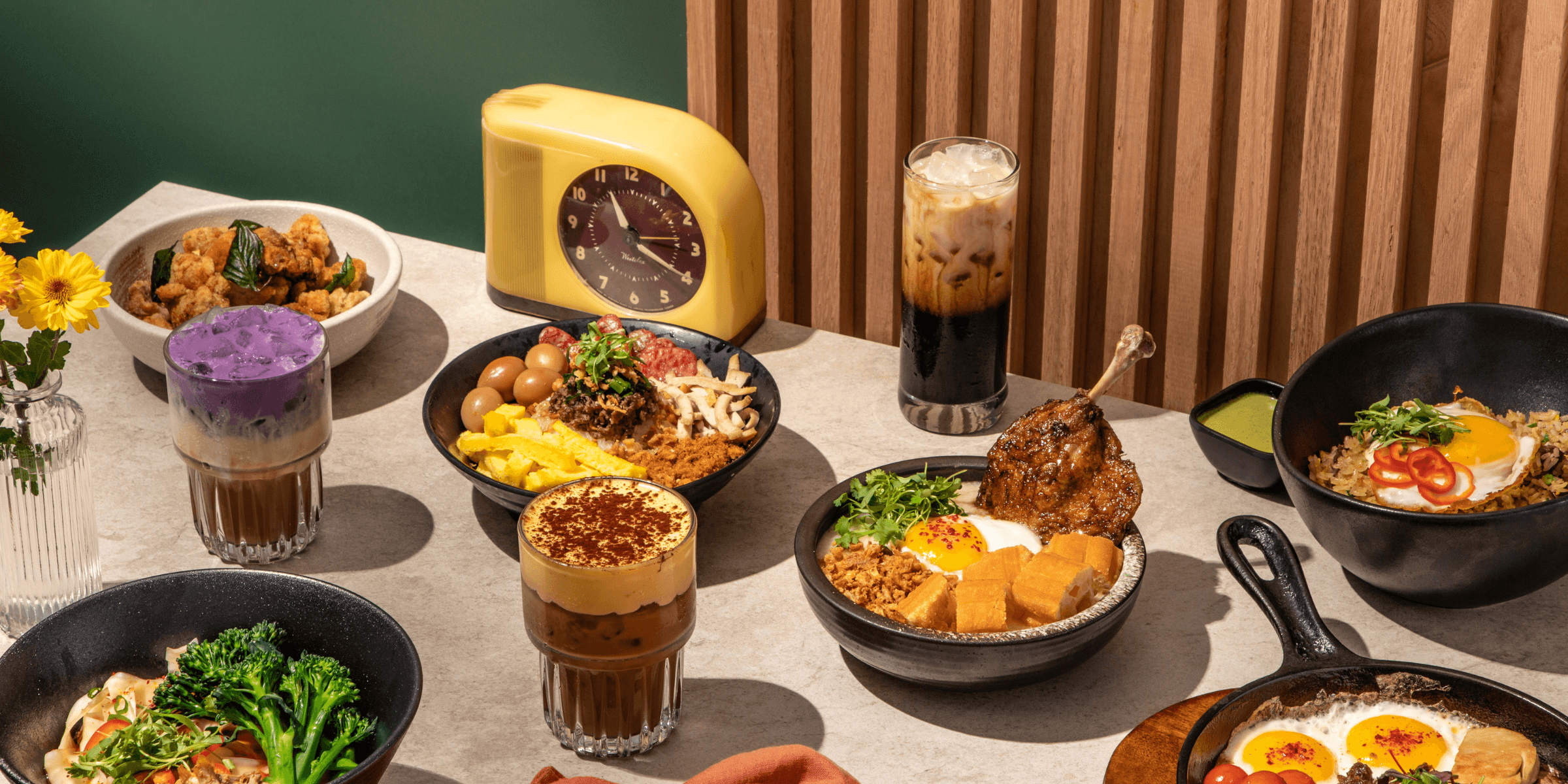 An overhead spread of Vietnamese-inspired dishes and drinks featuring banh mi chao with a sunny-side egg, beef tongue fried rice, egg coffee, ube coffee and other signature plates arranged on a modern table setting.