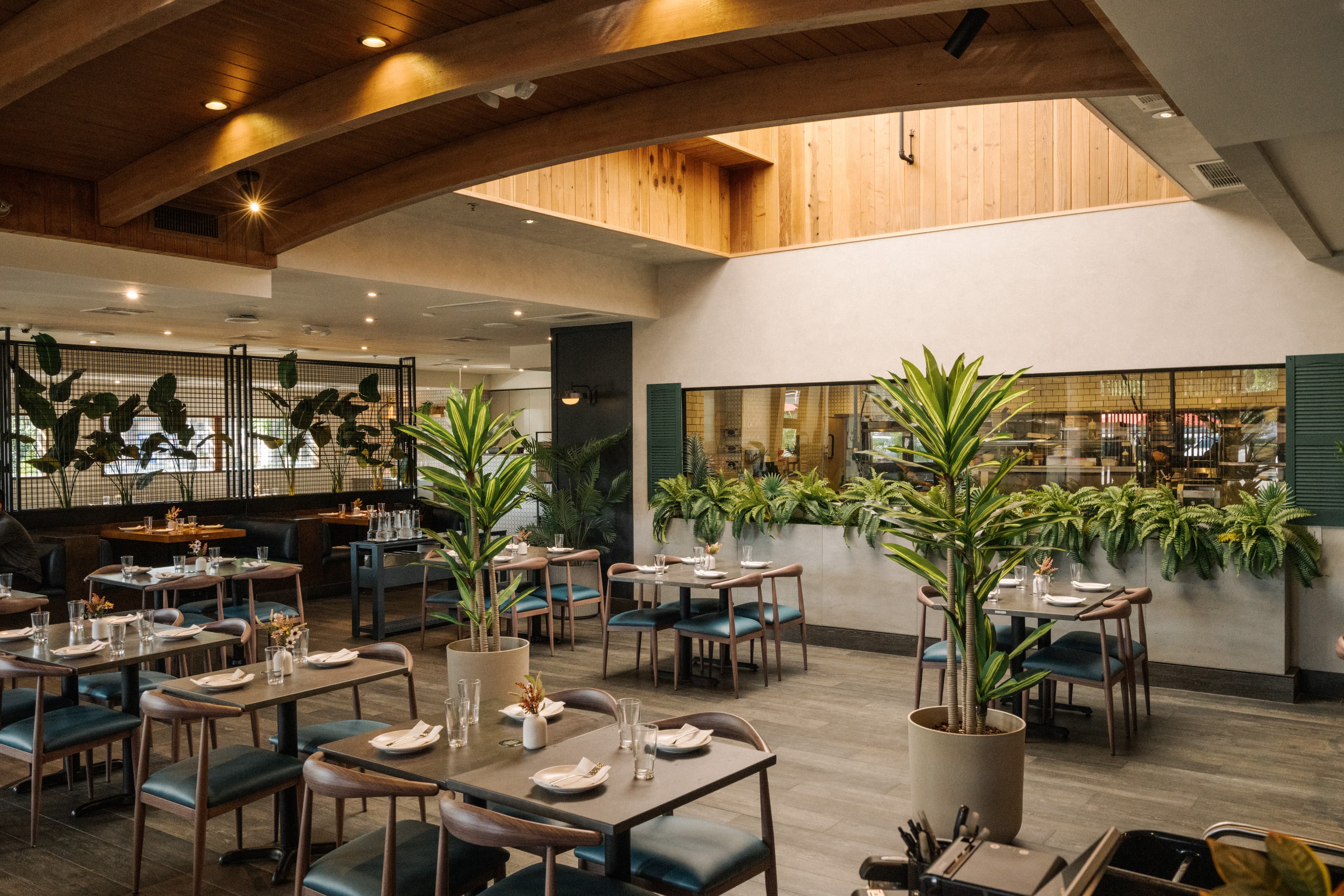 Interior of NEP Cafe’s Irvine location featuring a modern dining space with warm wood accents, lush greenery, contemporary seating, and softly lit tables arranged throughout the airy restaurant.